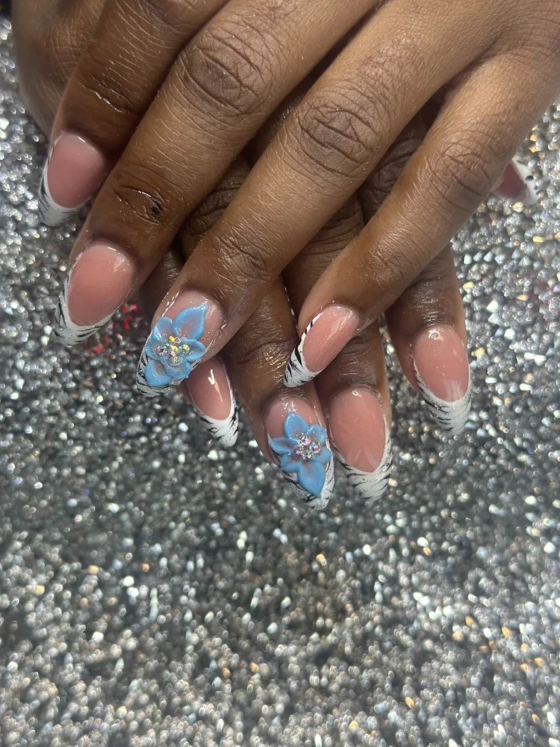 White zebra-stripe French tips with a hand-sculpted 3D blue flower and rhinestones